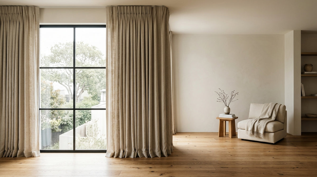 Floor-to-ceiling tailored pinch pleat curtains in natural textured linen framing soft daylight and cozy wooden flooring